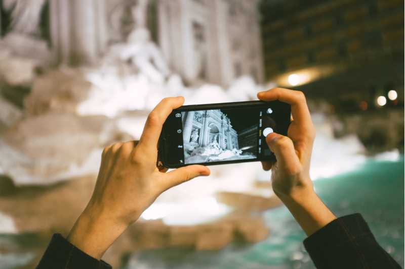 Photo: Two hands holding a mobile and photographing Fontana di Trevi in Rome.