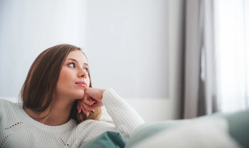 Kvinne sitter i sofa og ser ut av vindu